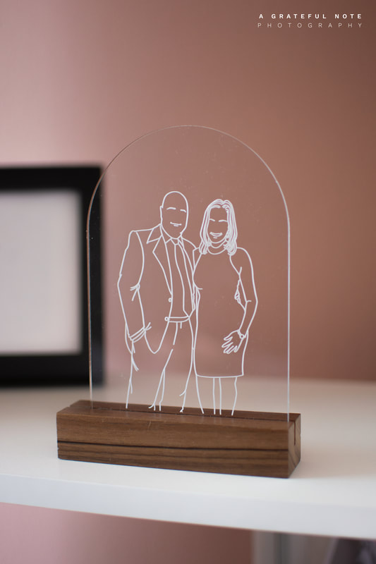 Couple Portrait Drawing in Fine Line Illustration style. The image is engraved on Clear Acrylic Frame and displayed on a Wooden holder.