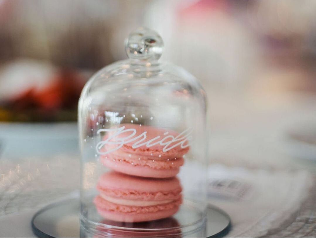 Glass dome with name in modern calligraphy style, covering pink macaroons on table 